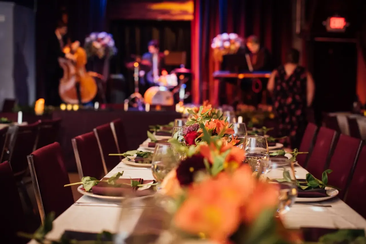 Table set with white linens and floral centerpieces in front of a band on stage at The Hook and Ladder, arranged for a private event